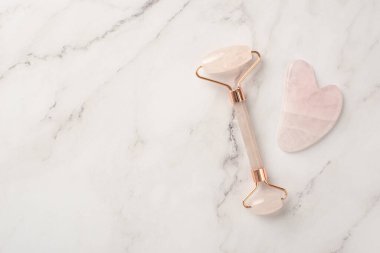 Cilt bakımı. Beyaz mermer zemin üzerinde gül kuvars silindiri ve gua sha masajcısı telif alanı ile üst görünüm fotoğrafı
