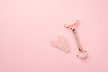 Güzellik prosedürü konsepti. Gül kuvars silindiri ve gua sha 'nın izole edilmiş pastel pembe arkaplandaki telif alanı ile en üstteki görüntüsü