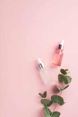 Güzellik prosedürü konsepti. Üst görüntüde iki şeffaf pembe ve beyaz damlacık şişesi ve okaliptüs, izole edilmiş pastel pembe arka planda, kopyalanmış