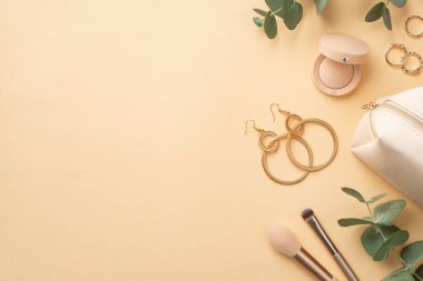 Güzellik konsepti. Altın yüzüklerin üst görünümü küpeler makyaj fırçaları kozmetik çanta ve izole edilmiş pastel bej arka plan üzerinde okaliptüs