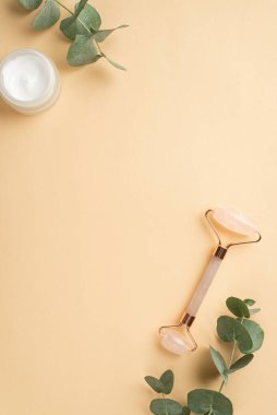 Cilt bakımı. Yalıtılmış pastel bej arkaplan üzerinde gül kuvars krem kavanozu ve okaliptüs dikey fotoğraf ortada telif alanı