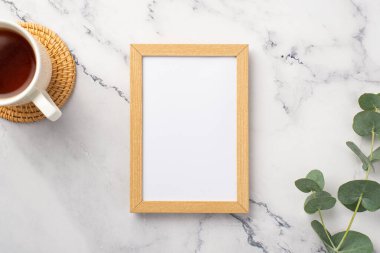 Çayın en üstteki görüntüsü rattan servis edilmiş ahşap fotoğraf çerçevesi ve beyaz mermer zemin üzerinde okaliptüs boş alan.