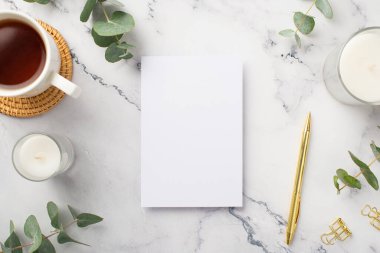 Kağıt çarşaf mumlarının en üstteki fotoğrafı rattan servis edilmiş çay fincanı altın kalem ataçları ve beyaz mermer arka plan üzerinde okaliptüs boş alan