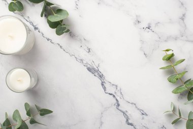 Top view photo of candles with glass holders and eucalyptus on white marble background with copyspace