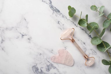 Okaliptüs 'ün üst görüntü fotoğrafı gül kuvars silindiri ve gua sha masaj aleti beyaz mermer arka planda boş alan
