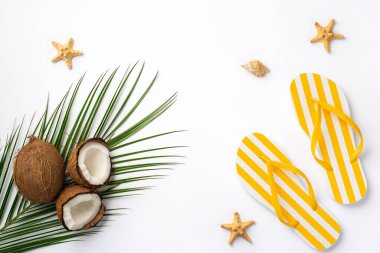 Yaz kavramı. Sarı çizgili terliklerin, hindistan cevizi balıklarının kabuk ve palmiye yapraklarının izole edilmiş beyaz arka planda en üstteki fotoğrafı.