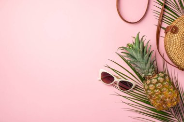 Summer vacation concept. Top view photo of pineapple round rattan bag sunglasses and palm leaves on isolated pastel pink background with copyspace
