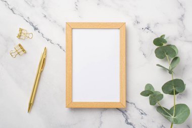 İş konsepti. Tahta fotoğraf çerçevesi, altın kalem ataçları ve beyaz mermer zemin üzerinde okaliptüs filizi, boş alan.