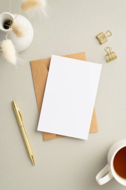 İş konsepti. Kağıt kaplama kağıdın dikey fotoğrafı. Kağıt zarf. Altın cilt. Çay ve vazo, pastel gri arka planda beyaz lagurus çiçekleri.