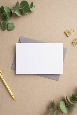 İş yeri konsepti. Kağıt yaprağının dikey resmi. Gri zarf. Altın kalem ataçları ve bej arkaplan üzerinde okaliptüs.