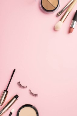 Makyaj konsepti. Üst görünüm palet ruj biçimlendirme dikey fotoğraf sahte kirpikler makyaj fırçaları rimel ve kompakt toz üzerinde pastel pembe arka plan fotokopi