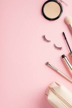 Güzellik konsepti uydur. Pudra kabı makyajının dikey üst görüntüsü boş alan arkaplanlı pastel pembe arka planda rimel, takma kirpik ve kozmetik çanta.