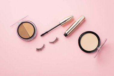 Güzellik konsepti uydur. Üst görünüm fotoğraf kompakt toz palet sahte kirpikleri ve rimel üzerinde pastel pembe arka plan