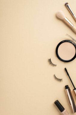 Makyaj konsepti. Makyaj malzemelerinin dikey üst görüntüsü, rimel takma kirpikleri ve telif alanlı pastel bej arka planda tırnak cilası.