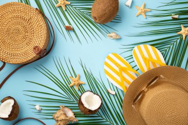 Yaz haftasonu konsepti. Yuvarlak çizgili çantanın üst görüntüsü sarı çizgili terliklerin güneş gözlükleri hindistan cevizi balığı kabukları ve izole edilmiş pastel mavi arka planda palmiye yaprakları.