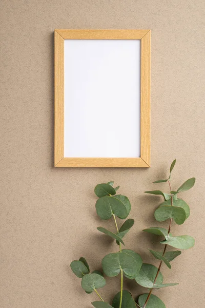 Bej renkli duvardaki ahşap fotoğraf çerçevesinin dikey fotoğrafı ve boş boşluklu okaliptüs dalları