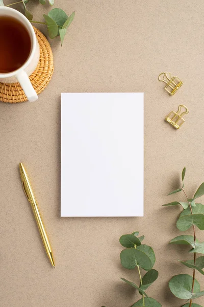 Kağıt yaprağının dikey resmi altın kalem cilt tokaları okaliptüs yaprakları ve bej arkaplan üzerinde rattan servis paspası üzerinde bir fincan çay