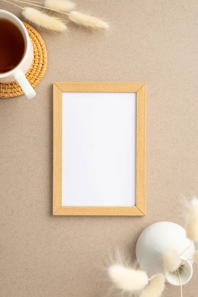 Ahşap fotoğraf çerçevesi, beyaz lagurus çiçekli seramik vazo ve bej arkaplan üzerinde servis paspası üzerinde çay fincanı.