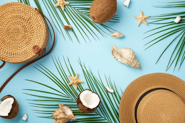 Yaz tatili konsepti. Yuvarlak rattan çantalı şapka, hindistan cevizi, deniz yıldızı kabuğu ve açık mavi arka planda palmiye yapraklarının en üst görüntüsü.