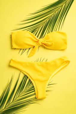 Yaz tatili konsepti. Sarı bikinili ve sarı arkaplanlı palmiye yapraklı üst görünüm dikey fotoğraf
