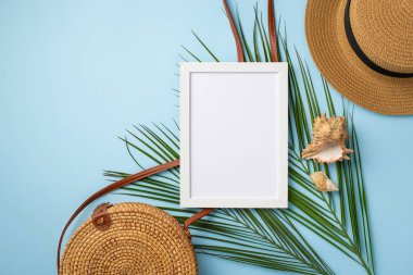 Yaz tatili konsepti. Beyaz çerçeveli şapkanın üst görünüm fotoğrafı rattan el çantası kabukları ve izole edilmiş pastel mavi arkaplan üzerinde palmiye yaprakları boş alan
