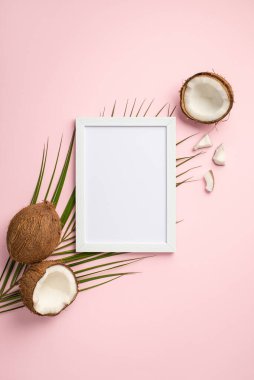 Yaz tatili konsepti. Beyaz fotoğraf çerçevesinin dikey üst görüntüsü çatlak hindistan cevizi ve palmiye yaprakları boş arkaplan ile izole pembe arkaplan üzerinde