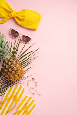 Yaz tatili konsepti. Sarı mayo korse güneş gözlükleri sarı çizgili terlikler ananas kabuklu bilezikler ve izole edilmiş pastel pembe arka planda palmiye yaprakları.