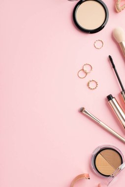 Makyaj güzellik konsepti. Üst görünümde altın yüzüklerin dikey fotoğrafı palet makyajlı bilezikler rimel fırçaları ve basınçlı toz ve pastel pembe arka planda fotokopi alanı