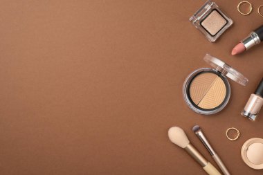 Makyaj güzellik konsepti. Göz fotografının üst görüntüsü: Palet altın yüzükler, makyaj fırçaları ve izole edilmiş kahverengi arka planda ruj.