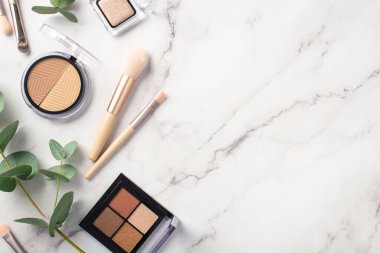 Makyaj konsepti. Makyaj fırçalarının beyaz mermer zemin üzerinde beyaz mermer paletler ve okaliptüsler çizen göz fotograflarının üst görünümü