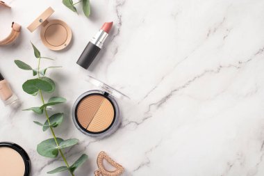 Makyaj konsepti. Palet göz fotografının üst görüntüsü kompakt toz ruj tırnak cilası altın bilezik saç tokası ve okaliptüs beyaz mermer zemin üzerinde kopyalanmış mermer alan