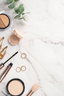 Güzellik konsepti uydur. Üst görünüm dikey fotograf konturing palet pudra makyaj fırça göz farı rimel altın halkalar tokalar ve beyaz mermer zemin üzerinde okaliptüs boş alan