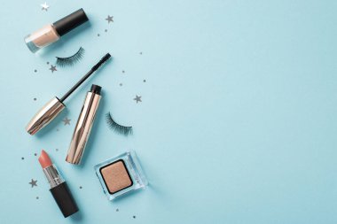 Makyaj konsepti. Üst görünümde sahte kirpiklerin maskara ruj sürme göz farı ojesi ve izole edilmiş pastel mavi arka planda parlak yıldız şekilli konfeti.
