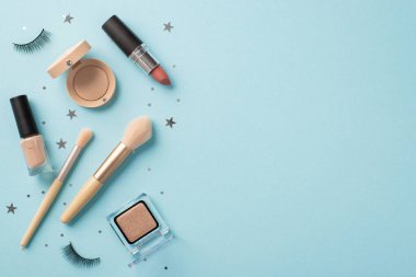 Makyaj güzellik konsepti. Sahte kirpiklerin üst görünüm fotoğrafı ruj makyaj fırçaları göz farı ojeleri ve izole edilmiş pastel mavi arka planda yıldız şekilli konfeti boş alan.