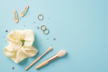 Makyaj güzellik konsepti. Makyaj fırçalarının, saç tokalarının, altın yüzüklerin ve izole edilmiş pastel mavi arka planda parlak yıldız şekilli konfetilerin üst görüntüsü.