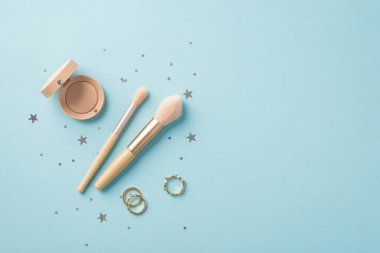 Makyaj konsepti. Üst görüntüde iki makyaj fırçası göz farı konteynırı altın halkalar ve izole edilmiş açık mavi arka planda yıldız şekilli konfeti.