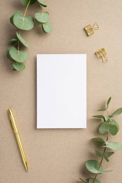 Kağıt kart, kalem ataçları ve bej arkaplan üzerindeki okaliptüslerin dikey görüntüsü boş arkaplan