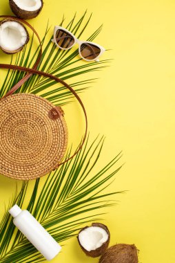 Yaz kavramı. Yuvarlak rattan çantanın dikey fotoğrafı güneş gözlüğü kırık hindistan cevizleri ve izole edilmiş sarı arka planda palmiye yaprakları.