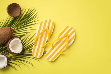 Yaz tatili konsepti. Sarı çizgili parmak arası terliklerin üst görüntüsü hindistan cevizi ve palmiye yaprakları kopyalanmış sarı arka planda