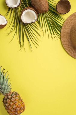 Yaz tatili konsepti. Güneş şapkalı, tropikal meyvelerin dikey fotoğrafı ananas ve yeşil palmiye yaprakları izole edilmiş sarı arka planda boş alan.