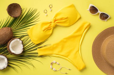 Yaz tatili konsepti. Sarı bikini şapkalı şık güneş gözlüklü bilezik küpeli hindistan cevizi ve sarı arka planda palmiye yapraklı fotoğraf.