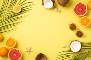 Yaz kavramı. Güneş gözlüklü deniz yıldızı kabuğu tropikal meyveler kırılmış hindistan cevizleri portakal, greyfurt ve palmiye yaprakları izole edilmiş sarı arka planda ve ortası kopyalanmış