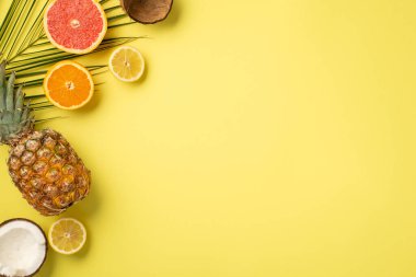 Yaz haftasonu konsepti. Tropikal meyvelerin, hindistan cevizi dilimli portakal limonlu greyfurt ananasının ve izole edilmiş sarı arka planda boş alan olan palmiye yapraklarının üst görüntüsü.