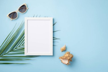 Yaz tatili kavramı. İzole edilmiş pastel arkaplanda beyaz fotoğraf çerçevesi güneş gözlüğü kabukları ve palmiye yaprakları boş alan ile mavi arkaplan
