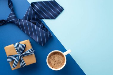Babalar Günü konsepti. El işi kâğıdı hediye kutusunun üst görüntüsü. Kurdeleli papyon, köpüklü kahve fincanı ve iki renkli mavi arka planda, kopyalanmış mavi kravat.