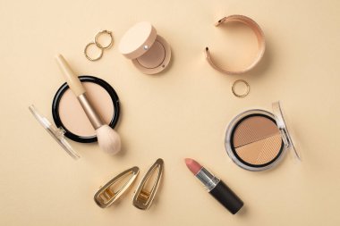 Uydurma konsept. Üst görünüm fotoğraf daire bileşimi ruj kompakt toz fırça çerçeve palet göz farı altın bileklik halkalar ve tokalar pastel bej arkaplan üzerinde