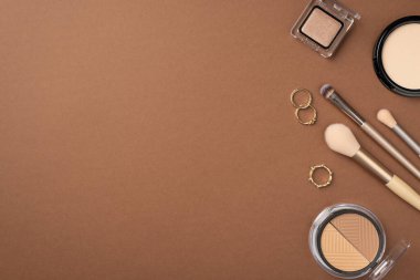 Uydurma konsept. Üst görünüm fotoğraf konturing palet göz falı kompakt toz altın halkalar ve izole kahverengi arka planda makyaj fırçaları