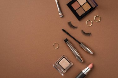 Makyaj konsepti. Göz fotografı palet makyaj fırçası altın halkalar ruj rimel ve izole edilmiş kahverengi arka planda takma kirpiklerin üst görünümü