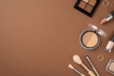 Makyaj konsepti. Göz farı ve konturlu paletlerin üst görünüm fotoğrafı altın yüzükler makyaj fırçaları ve izole edilmiş kahverengi arka planda ruj
