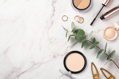 Makyaj güzellik konsepti. Üst görünüm fotoğraf palet göz kaplaması rimel altın halkalar tokalar ve okaliptüs yaprakları beyaz mermer arka plan üzerinde telif alanı ile